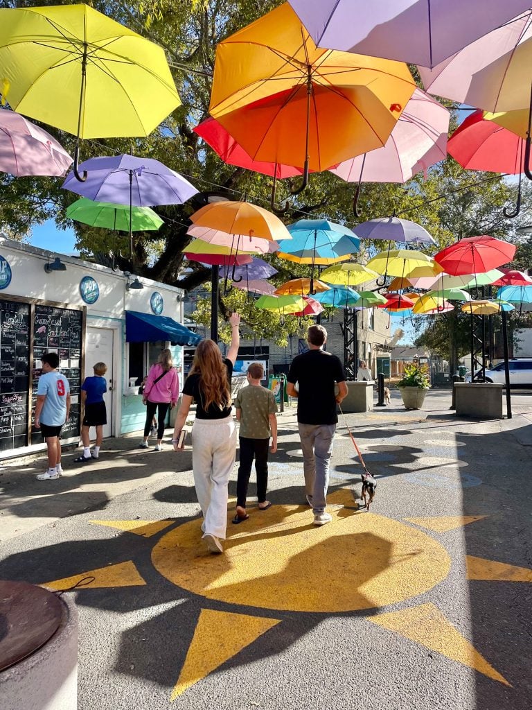 ocean-springs-cash-alley-umbrellas-768x1024-1 Kids Walking Under Bright Umbrellas In Cash Alley In Ocean Springs Mississippi