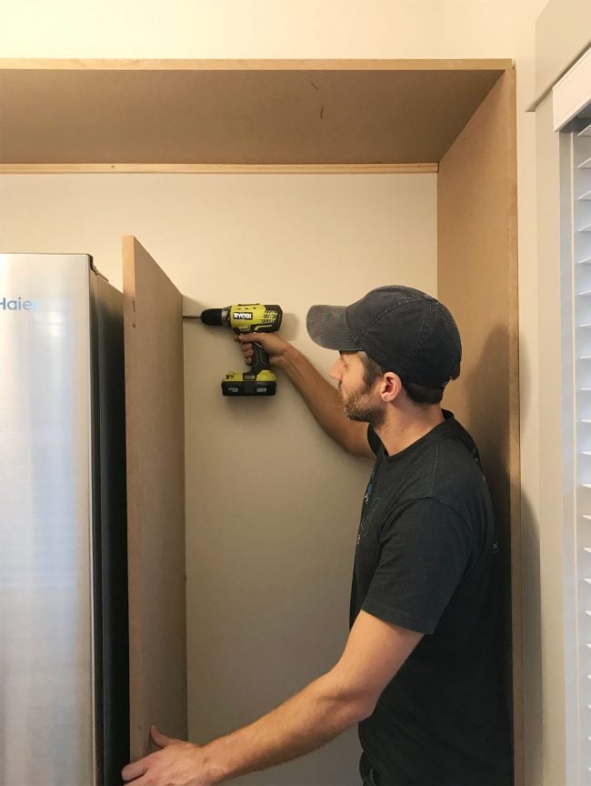 beach-beach-house-john-securing-side-piece-650x864-1 John drilling vertical MDF panel into wood already placed near fridge in pantry
