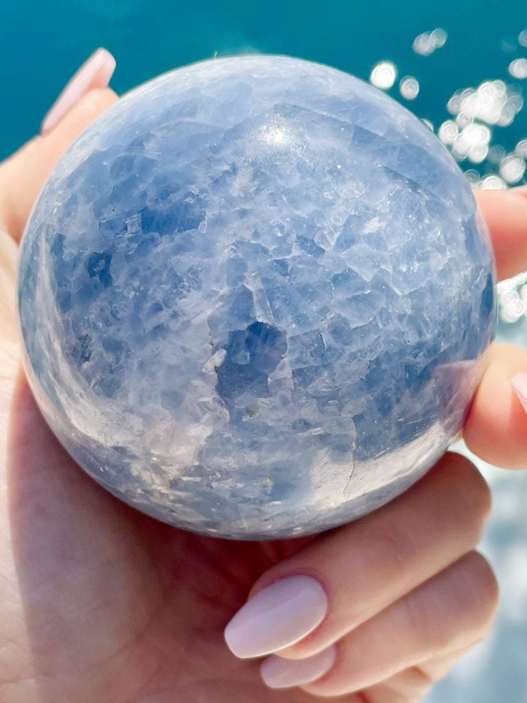 blue-calcite-crystal-orb-in-hand-768x1024-1 Blue Calcite Crystal Sphere Over Water