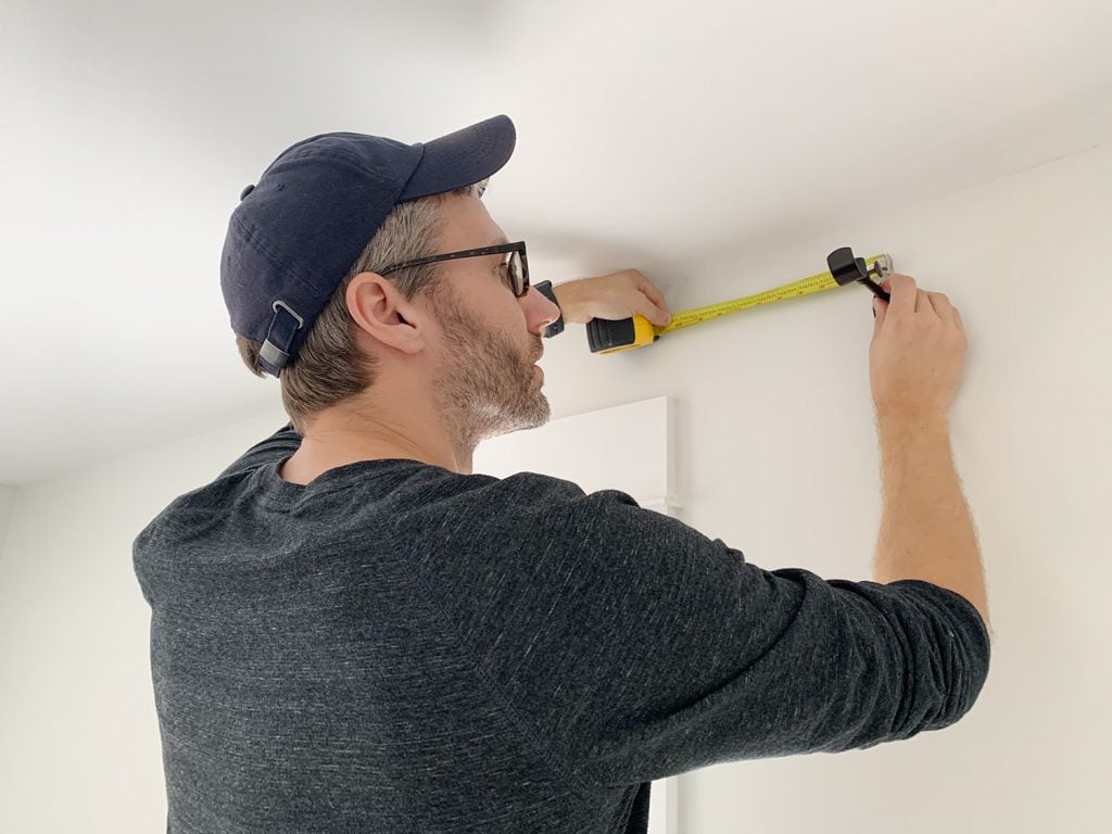 hanging-curtain-rods-john-measuring-placement-1024x768-1 John measuring wall above window while holding curtain rod hook