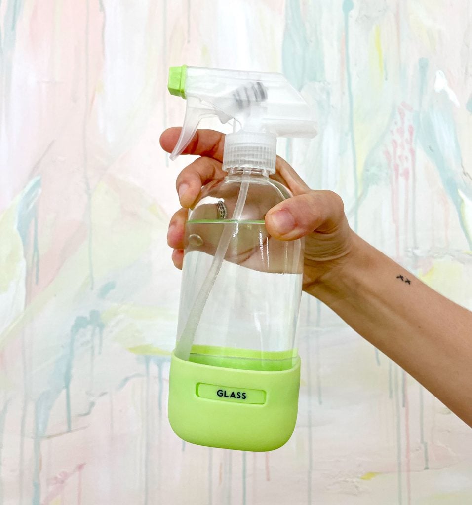 homemade-glass-cleaner-in-front-of-painting-956x1024-1 Hand Holding Homemade Window Cleaner In Glass Bottle In Front Of Colorful Painting