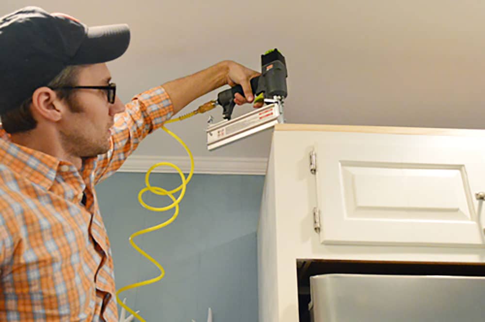 kitchen-crown-john-nailing-scrap-in John using nail gun to attached scrap wood to top of cabinet