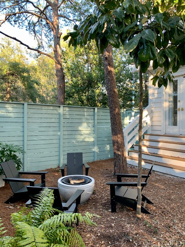 firepit-after-vertical-angled-shot-768x1024-1 Trees around fenced side yard with black Adirondack chairs around fire pit