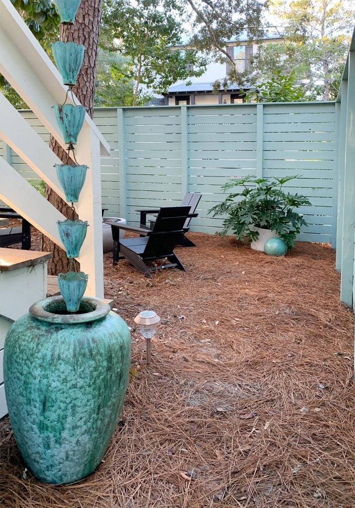 firepit-area-facing-in-from-gate-717x1024-1 View through gate fence next to blue-green pot and rain chain