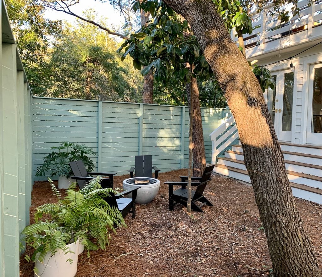 firepit-area-horiztonal-side-area-wider-1024x881-1 Green fenced side yard with black Adirondack chairs around fire pit