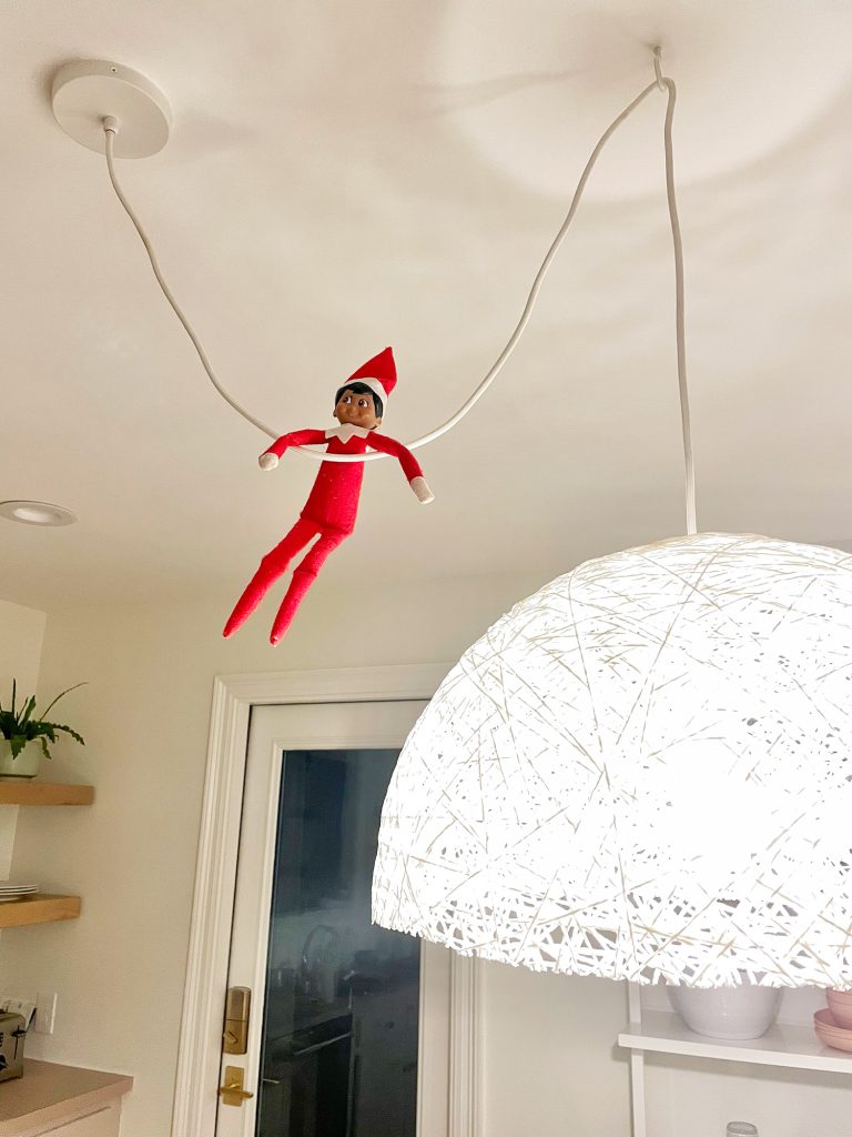 holiday-house-elf-on-the-shelf-768x1024-1 Elf on the Shelf hanging from pendant light cord in kitchen