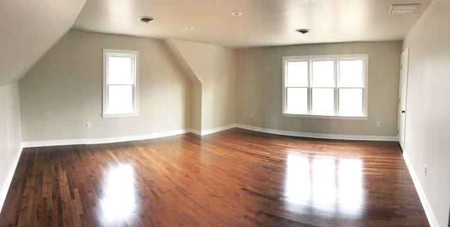 image Wide angle panoramic photo of an empty bonus room with tan walls, wood floor, windows, and niche nook