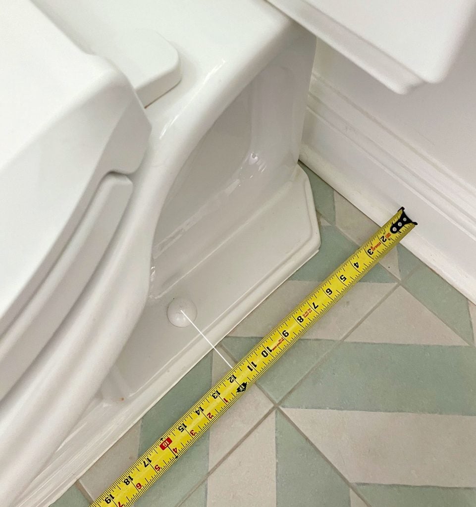 install-a-toilet-rough-in-tape-measure-961x1024-1 Tape Measure Taking Rough In Measurement By Toilet Bowl
