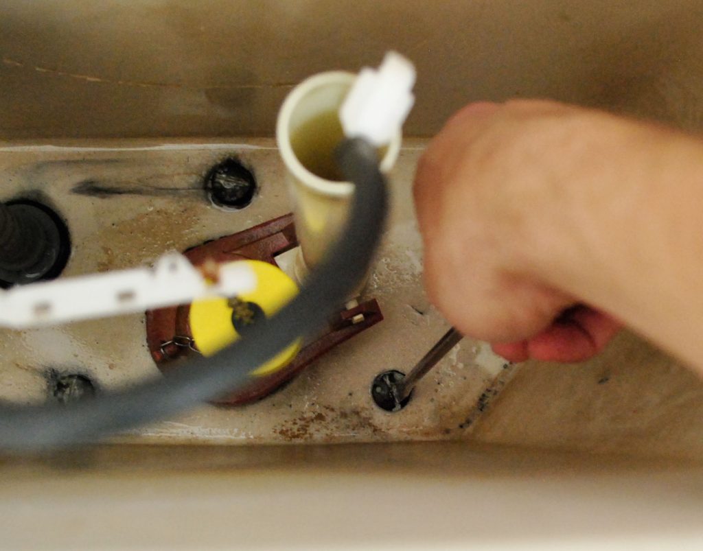 install-a-toilet-unscrewing-tank-1024x803-1 Hand With Screwdriver Adjusting Bolts In Toilet Tank