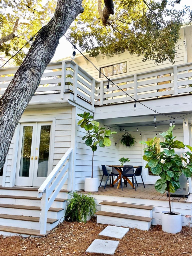 kitchen-porch-vertical-after-768x1024-1 View of side porch with large oak tree in foreground with white house string lights and fig trees