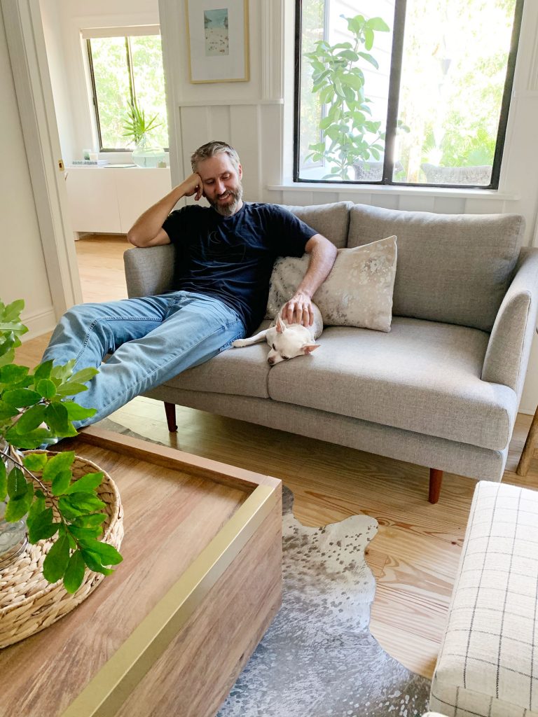 loveseat-john-for-scale-768x1024-1 John sitting on gray loveseat with chihuahua next to him