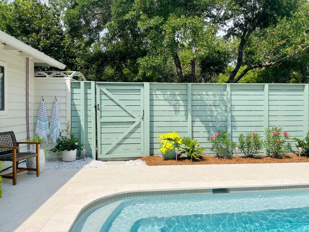 pool-post-horizontal-fence-gate-outdoor-shower-big-tree-over-fence-1024x768-1 Pool fence with horizontal slats and gray green paint with planting bed in front