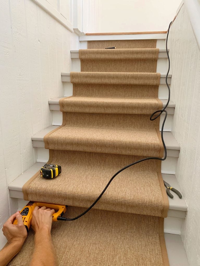 sisal-stair-runner-nailing-under-lip-768x1024-1 Hand Pushing Electric Stapler Into Underside Of Stair Tread To Secure Sisal Runner